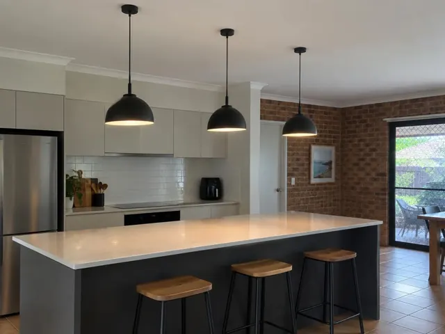 Three black pendant lights above a kitchen island in a modern brick and tiled home interior in Varsity Lakes