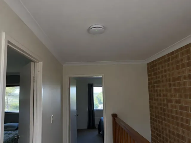 Ceiling smoke alarm in a hallway with cream walls and a brick feature wall in Reedy Creek